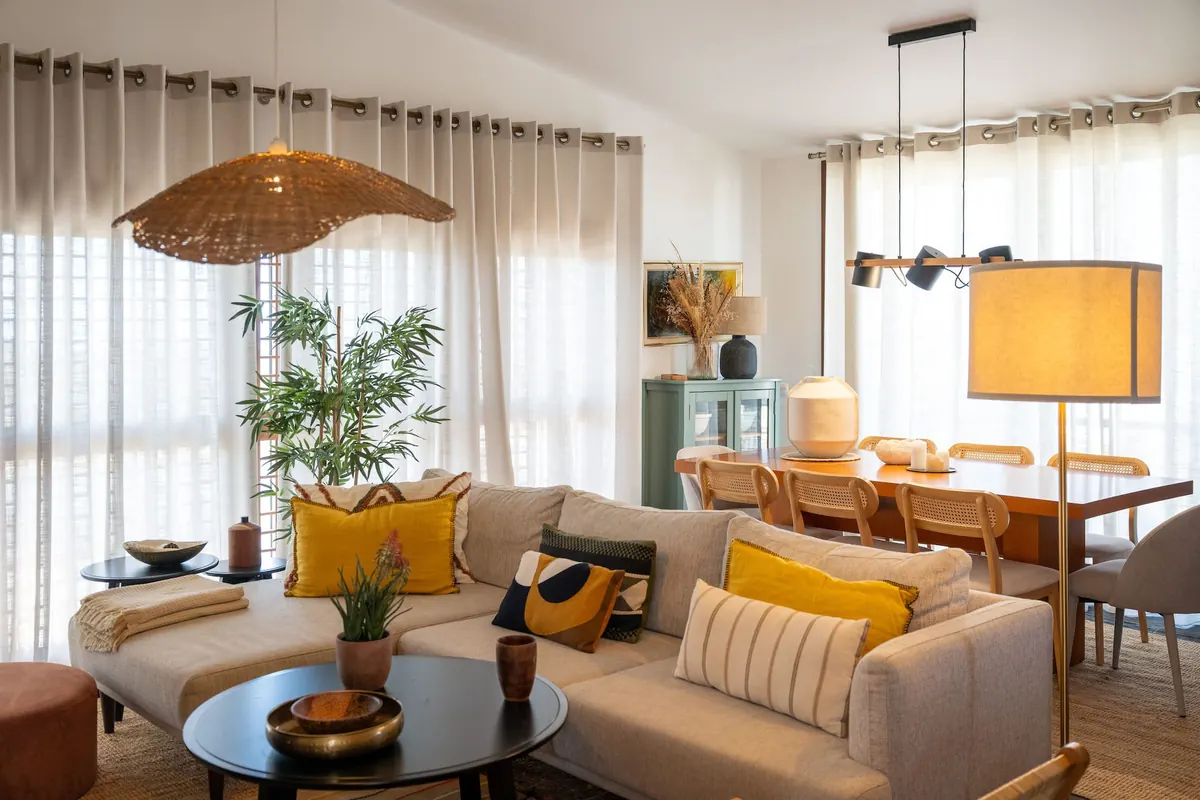 Sala de estar com sofás claros, almofadas em tons de ocre e zona de refeições ao fundo