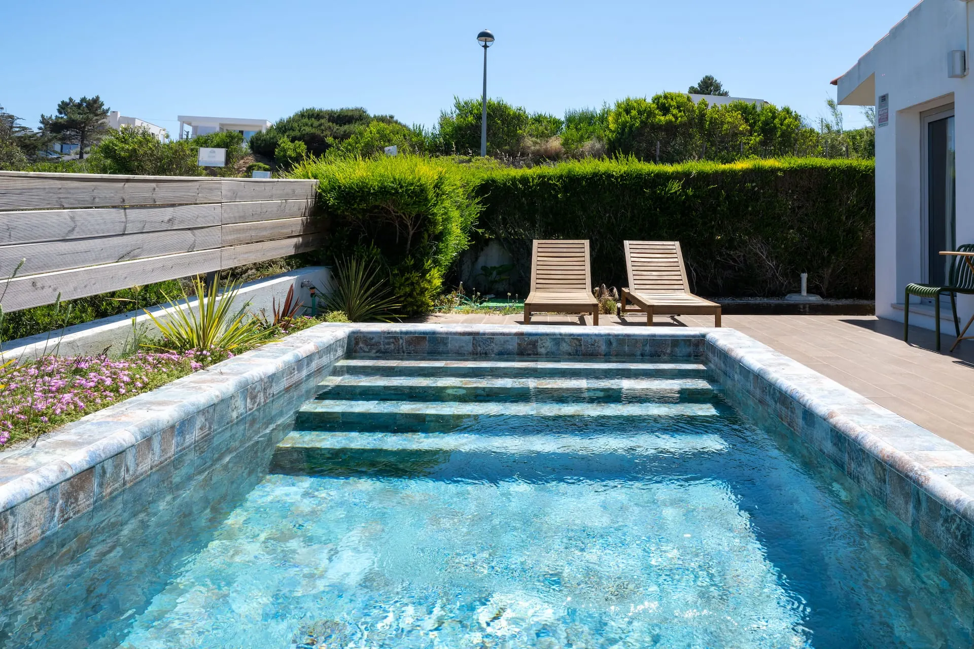 Piscina privada com espreguiçadeiras, rodeada por muro de pedra e vegetação