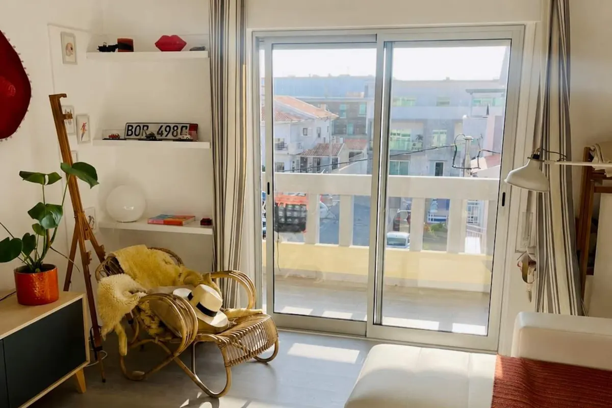 Sala luminosa com porta envidraçada para a varanda e tapete às riscas azuis