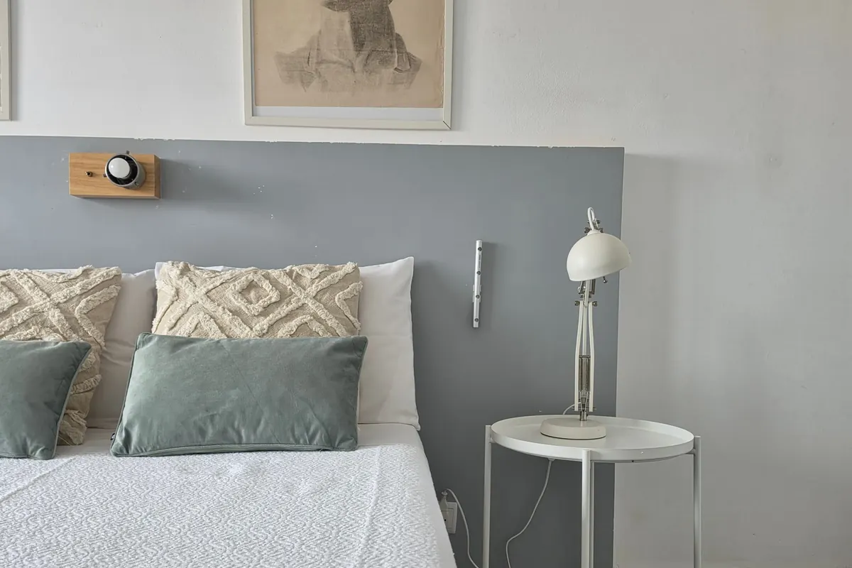 Quarto com cama de casal, colcha verde e candeeiro de leitura