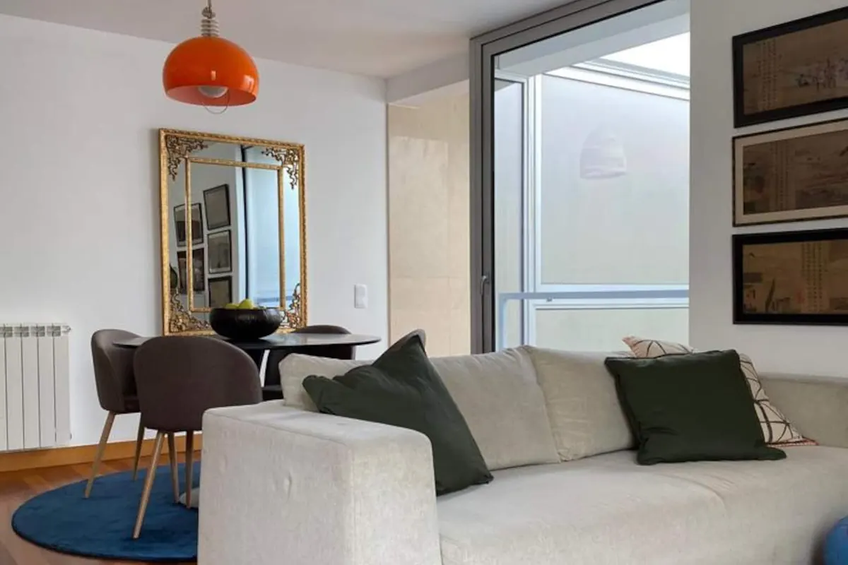 Sala com sofá branco, tapete persa e candeeiro suspenso cor de laranja, sobre soalho de madeira